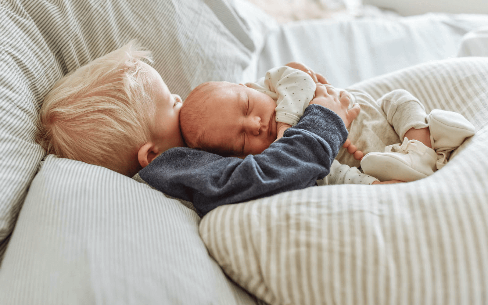 New big brother holding a newborn resting on a linen nursing pillow cover with pillow.